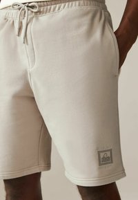 Lysbeige shorts lavet af blødt stof, med en elastisk talje med snore og sidelommer. Inkluderer et trykt Miami Coast-logo.