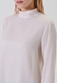 Helles pinkes Bluse mit hohem Kragen, langen Ärmeln und einer glatten, leicht reflektierenden Textur. Einfaches Design ohne auffällige Muster oder Hardware.