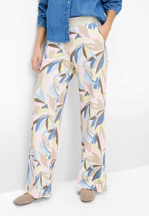 Person iført vidde bukser med pastel abstrakt bladprint, beige elastisk taljebånd, blå denimskjorte og beige slip-on sko.