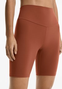 Höga, stretchiga cykelshorts i bränd orange färg. Slät textur med en åtsittande design, som når mitten av låret.