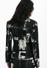 Black denim jacket featuring a collage of white text and graphics, with contrast stitching and structured design.