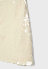 Tissu crème avec des paillettes blanches brillantes éparpillées créant une surface scintillante et texturée sur un textile doux.