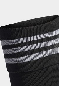 Calzino sportivo nero con texture a costine, dotato di strisce bianche orizzontali nella parte superiore, progettato per comfort e supporto.