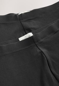 Zwei Paar schwarze Umstands-Leggings mit sichtbaren weißen Next maternity Etiketten am Bund, nah beieinander gefaltet.
