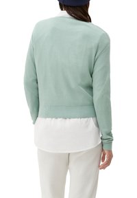 Maglione verde chiaro texturizzato con bordo a coste, indossato sopra una camicia bianca con colletto, caratterizzato da maniche lunghe e una vestibilità comoda.