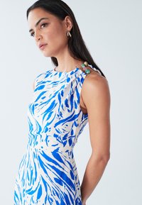 Fitted dress with a blue and white abstract pattern. Features a round neckline and decorative beads at the shoulder, made from lightweight fabric.