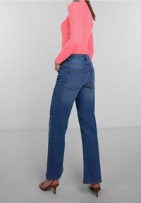 Blaue Jeans im weiten Bein mit hoher Taille, ausgestattet mit zwei Gesäßtaschen und sichtbaren Nähten. Getragen mit einem rosa gerippten Langarmoberteil.
