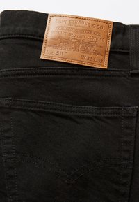 Poche arrière noire de jean Levi’s avec un patch en cuir marron indiquant la marque, la taille W32 L32 et les détails du lot 511.