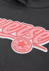 Γκρι βαμβακερό φούτερ με κουκούλα που διαθέτει μεγάλο ροζ λογότυπο "Converse" και ένα κόκκινο κυκλικό μπαλώμα με ένα αστέρι που περιλαμβάνει το κείμενο "Chuck Taylor" και "All Star".