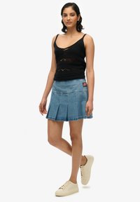 Top de tirantes finos en crochet negro combinado con una falda plisada de mezclilla azul clara. La falda tiene un parche con detalle de la bandera americana.