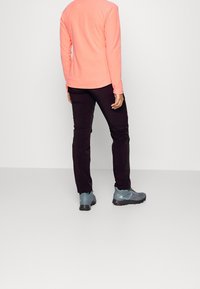 Kevyt, pitkähihaista kirkkaanpunaista fleece-paitaa yhdistetty tummiin housuihin ja harmaisiin vaelluskengiin. Sileä pinta, rento istuvuus, ilman kuvioita.