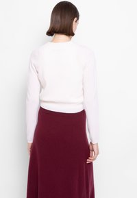 Maglione a maglia rosa chiaro con maniche lunghe, caratterizzato da un fondo aderente. Abbinato a una gonna lunga alla caviglia di colore bordeaux scuro, realizzata in tessuto morbido.