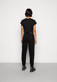 Camiseta negra de manga corta combinada con unos pantalones vaqueros negros de cintura alta. Los pantalones cuentan con una etiqueta de marca visible en la parte posterior y un corte recto.