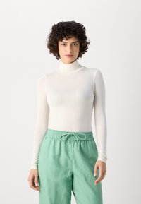 White long-sleeve turtleneck top paired with mint green loose-fitting pants. Top made of soft fabric, featuring a fitted design and high neck.