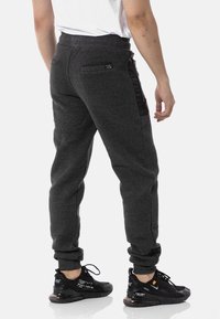 Dark gray joggers with a tapered fit, featuring a back pocket and side panel in shiny black material. Ribbed waist and cuffs.