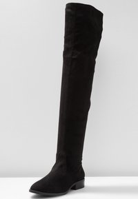 Botte noire cuissarde en daim doux, dotée d'un bout arrondi et d'un talon bloc bas pour plus de stabilité. Texture lisse, sans quincaillerie apparente.