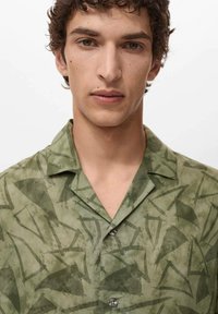 Camisa de manga corta verde hecha de una tela ligera, con un patrón abstracto en verde oscuro, cuello clásico y cierre frontal con botones.