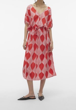 Kvinde iført en rød og hvid midi-kjole med bladmønster, snøre i taljen og sorte slingback-sko med spids tå.