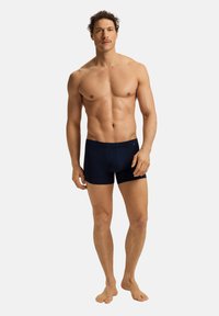 Bañadores de color azul marino con un diseño ajustado, fabricados con un material suave. Presentan una longitud hasta medio muslo y un logo sutil en la cintura.