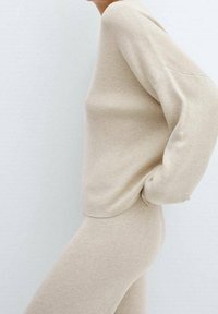 Pull en maille beige avec texture côtelée, coupe décontractée et manches longues, assorti à un pantalon en maille beige. Design simple et neutre.