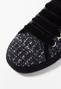 Texturerad svart skovupper med färgglada vävda mönster. Har svarta mocka-liknande snörningar och metallöglor för en säker passform.