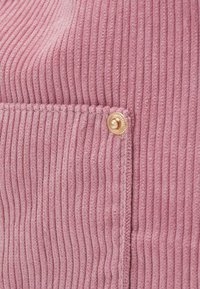 Gros plan d’un tissu en velours côtelé rose avec des rainures verticales et un petit bouton doré sur le coin d’une poche cousue.
