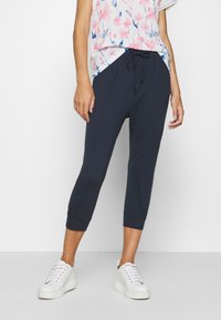 Marinenblå sweatshirtbyxor med elastiskt midjeband och muddar, med sidofickor. I kombination med en blommig topp och vita plattformssneakers.