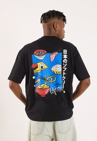 Sort t-shirt med et farverigt grafisk motiv på ryggen, der skildrer forskellige japanske retter mod en blå baggrund med hvide tekst-accenter.