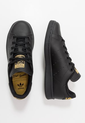 Paire de baskets Adidas Stan Smith noires avec lacets noirs, marquage doré sur la languette et le talon, vues de dessus et de côté sur fond blanc.