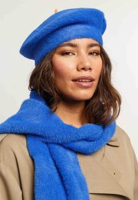 Sinine villane beret ja sobiv salli pehme, karvane tekstuur. Sall on mähitud kaela, koos beezist mantliga.