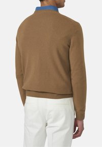 Pull en laine marron avec un col et des poignets côtelés, associé à un pantalon blanc. Détail notable du col bleu visible de dos.