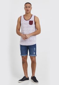 Ermeløs tanktopp med mørkerød kant, mønstret i lyse nyanser, og en lomme. Kombinert med oppbrettede jeansshorts og svarte joggesko.