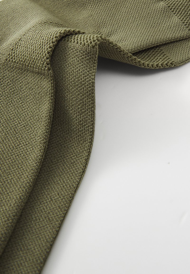 Olivgrüner Strickstoff mit strukturierten Oberflächen, gefaltet, um seine wellenförmige Form und die Nähdetails zu zeigen.