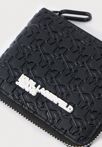 Black wallet in textured material featuring embossed logo patterns. Closure with metallic zipper and white "KARL LAGERFELD JEANS" lettering.