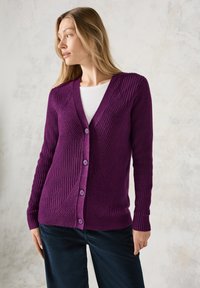 Fialový žebrovaný cardigan s výstřihem do V, který má diagonální vzory a pět knoflíků vpředu. Materiál vypadá měkce a má texturu.