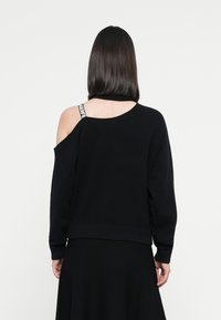 Black sweater with an off-shoulder design, ribbed hem, and long sleeves. Features a white branded strap visible on the shoulder.