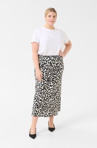 Falda midi de estampado de leopardo en crema y negro, hecha de un tejido ligero. Combinada con una camiseta blanca sencilla y tacones de punta negros.