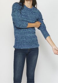 Pull en tricot texturé bleu à manches trois-quarts, col rond et coupe décontractée, associé à un jean en denim foncé.