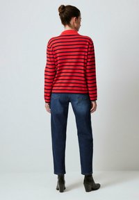Randig röd och marinblå tröja med långa ärmar och rundad halsringning, tillsammans med högmidjade mörkblå jeans och svarta ankelstövlar.