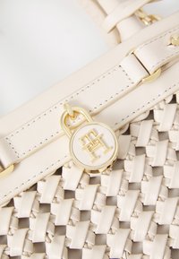 Πλεκτή μπεζ δερμάτινη τσάντα χειρός με κλείσιμο χρυσού τόνου και μενταγιόν λογότυπου. Λείες δερμάτινες λεπτομέρειες στη θήκη και στην τσάντα.