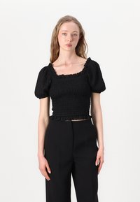 Crni smocked crop top s napučenim rukavima, kvadratnim izrezom i volanima na rubu. Materijal izgleda teksturirano s rebrastom završnom obradom.