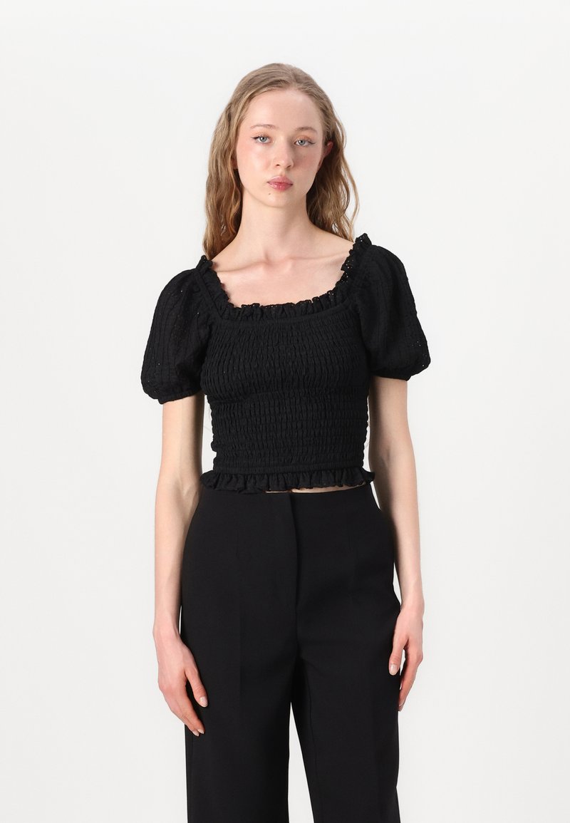 Crni smocked crop top s napučenim rukavima, kvadratnim izrezom i volanima na rubu. Materijal izgleda teksturirano s rebrastom završnom obradom.