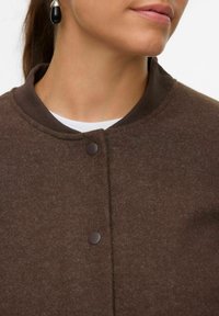 Veste en feutre marron avec un col rond, fermeture à boutons et col côtelé. Texture lisse avec des variations de couleur subtiles.
