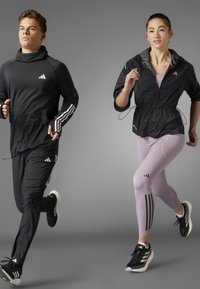 Crne sportske majice i hlače s bijelim Adidas trakama; ružičaste tajice s crnim trakama; oboje nosi crne tenisice za trčanje.