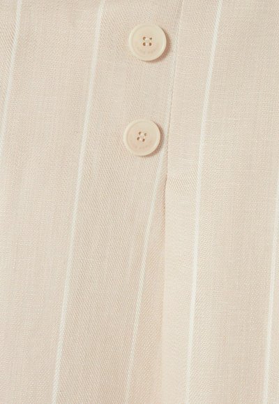 Tessuto beige chiaro con sottili righe sottili, caratterizzato da due bottoni chiari. La texture appare liscia e delicata.