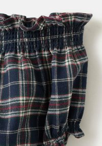 Navy blue plaid top with a gathered neckline. Features white and red lines, and smocked detailing at the shoulders and cuffs. Soft fabric texture.