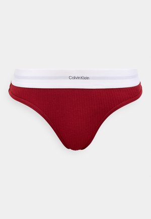 Tanga in cotone rosso a coste con elastico bianco in vita. Logo "Calvin Klein" sul fronte dell'elastico. Texture liscia.