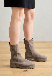 Taupe ankelstøvler med en glat suede-overflade, der har lodrette syninger, en sidelukning og en kraftig gummisål.