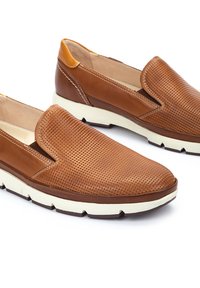 Zapatos marrones de cuero sin cordones con textura perforada, suela de goma beige clara y acentos en contraste de tan en el tacón.