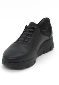 Zapato negro de cuero tipo slip-on con punta redondeada, acentos elásticos texturizados y suela de goma gruesa. Sin marcas visibles.